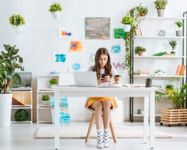 image of pretty young woman using a smartphone while sitting in a spacious beautiful office space - How to Create an Inspiring, Uplifting Office Space
