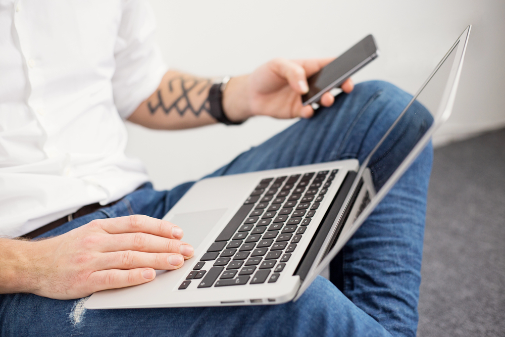 How Disposable SMS Numbers Can Enhance Your Online Verification Processes - man looking at his mobile device and laptop